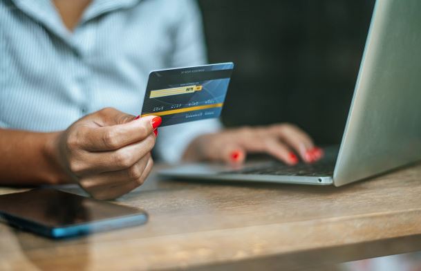 photo illustratrion of a person paying an online bill, credit card in hand in foreground, computer in the background