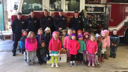 firemen posing with children in front of firetruck