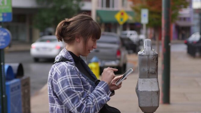Person using cellphone in front of parking meter