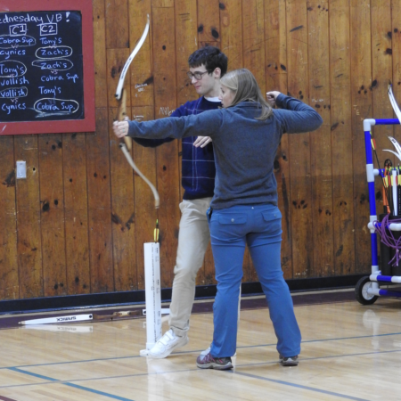 woman showing young man how to shoot bow