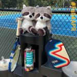 two stuff raccoons holding tennis and pickleball racquets