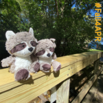 two stuffed raccoons sitting on wooden bridge railing