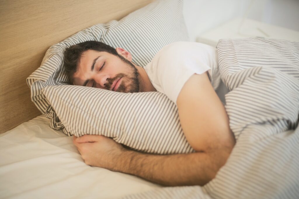 man sleeping in bed with arms wrapped around pillow