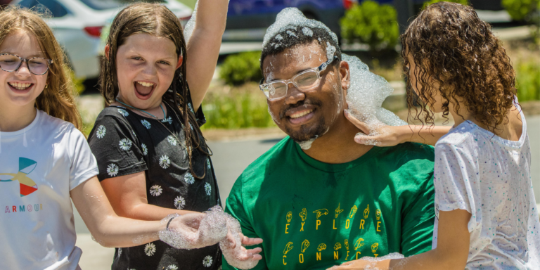 summer camp counselor playing in bubbles with 3 girls