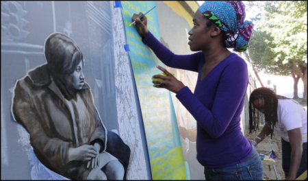 young black female artist painting on wall mural