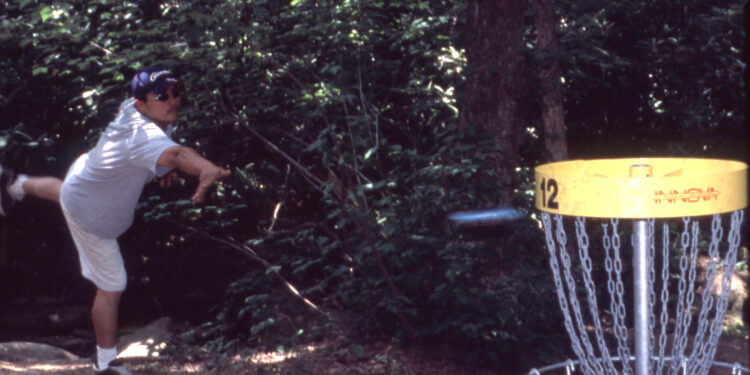 man throwing disc at target in wooded area