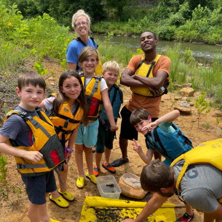 young people in life vests along the bank of a river