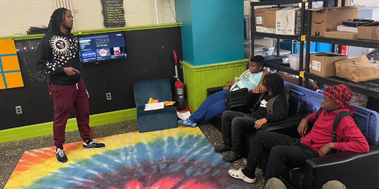 man speaking to young adults sitting in chairs