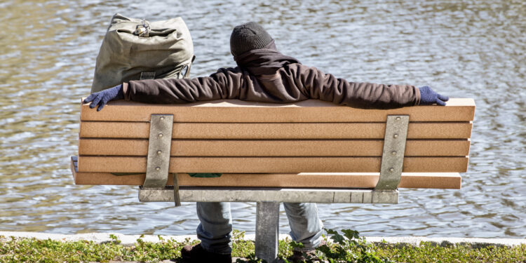 man sitting on bench by lake as seen from the back