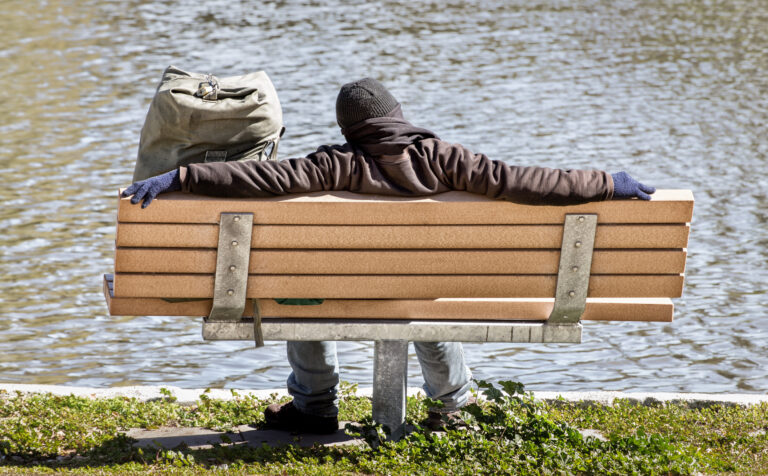 man sitting on bench by lake as seen from the back