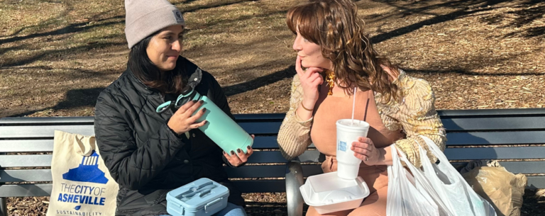two women sitting on bench, one holds reusable water bottle, the other holds styrofoam cup