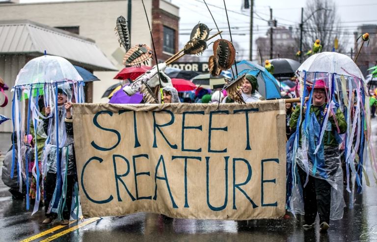 Parade members holding sign that reads street creature