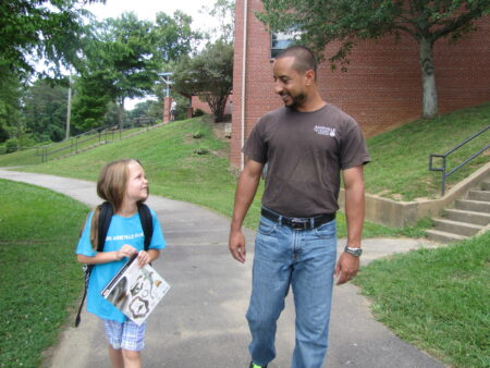 APR staff walking with child wearing a backpack outside of a community center