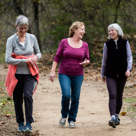 three middle aged women walking, talking, laughing on path in the woods