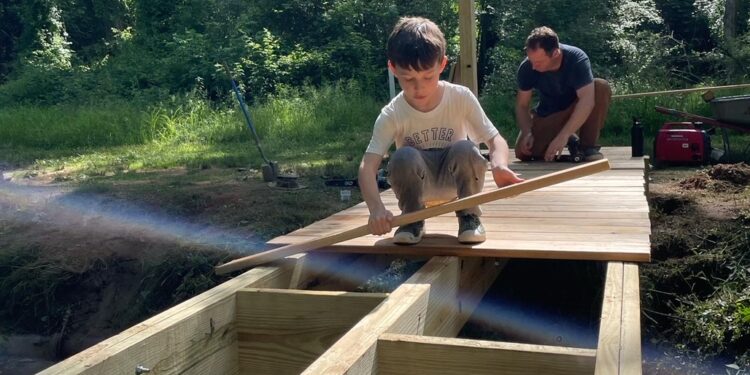 Photo of Drew Reisinger with his son, Simon, constructing a footbridge over Canie Creek in Asheville, NC.