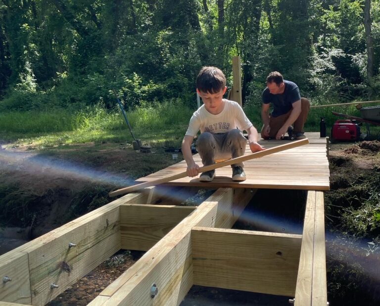 Photo of Drew Reisinger with his son, Simon, constructing a footbridge over Canie Creek in Asheville, NC.