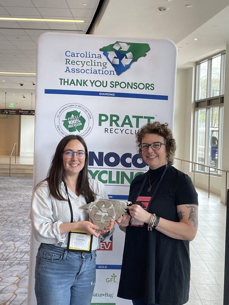 Jes Foster and Buncombe County employee holding the award in front of the event banner