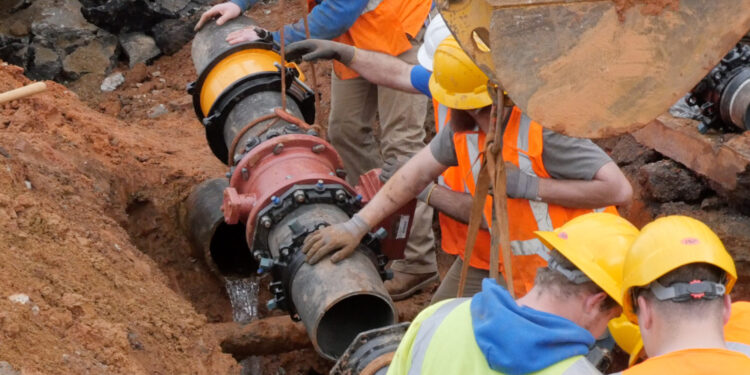 crew of workers wearing safety vests and hard hats repairing water line below surface level
