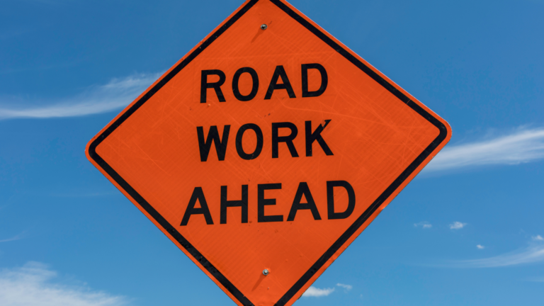 orange road sign with the text road work ahead