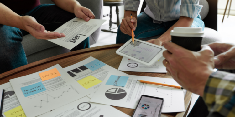 3 people sitting around a table looking at paper with graphs and charts