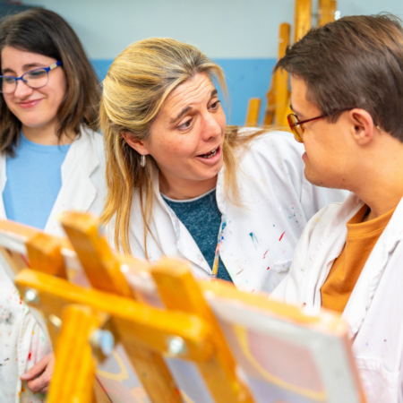 woman and young man wearing painters smocks standing in front of easel