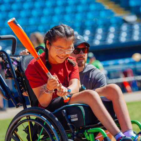 young Asian American girl in wheelchair holding baseball bat