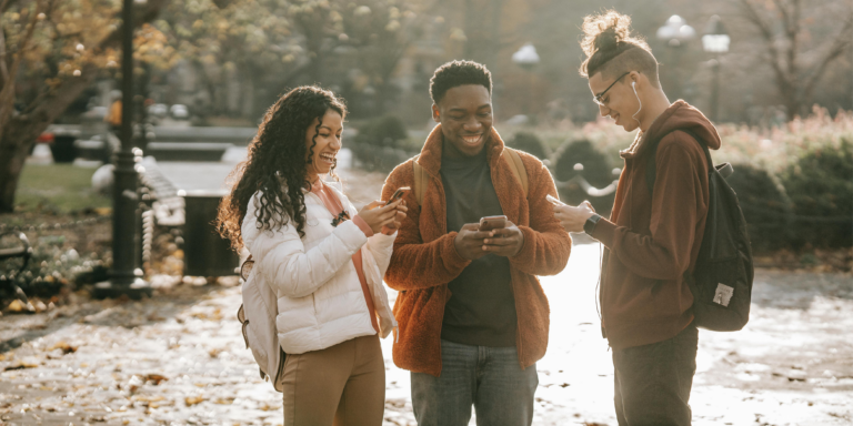three young people chatting while holding digital devices