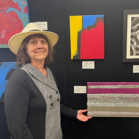 woman wearing hat displays artwork on black background wall