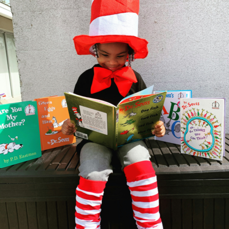 young child wearing dr. seuss costume reading dr. seuss books