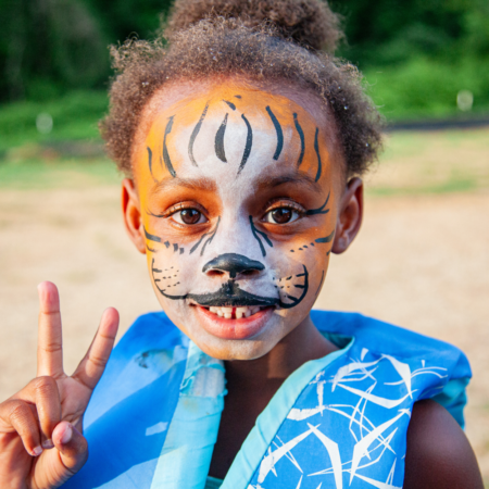 young girl wearing blue vest with face painted like a tiger
