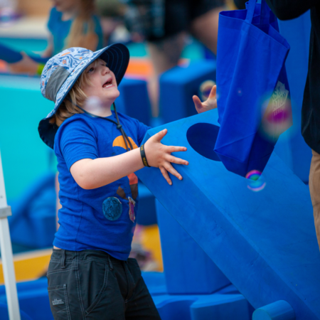 young boy in blue shirt wearing blue hat playing with blue foam blocks