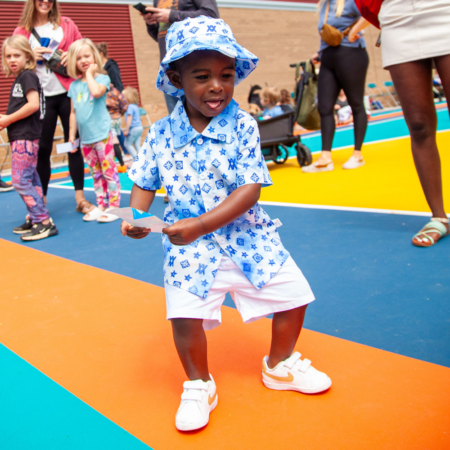 young boy wearing blue and white shirt and white shorts on colorful outdoor court