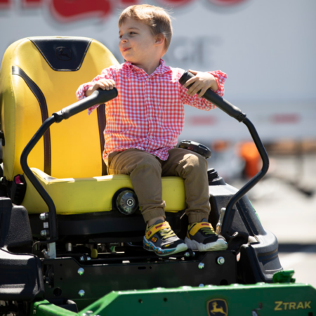 young boy in red plaid shirt on riding lawnmore