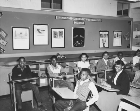 black and white photo of girls and boys in classroom sitting in desks