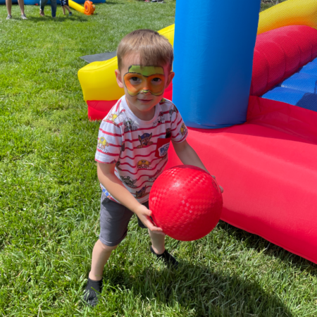 young boy holding red ball near inflatable