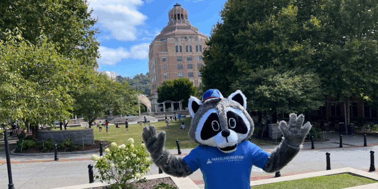raccoon mascot standing in front of city hall in pack square park