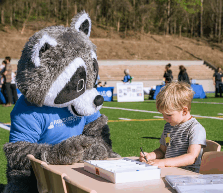 raccoon mascot with small child at table