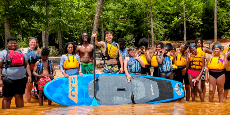 team of community posing for a picture in the river with a. paddle board