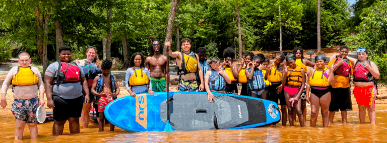 team of community posing for a picture in the river with a. paddle board