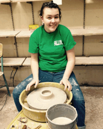 Fallon Hyder wears green tshirt and sits behind pottery wheel