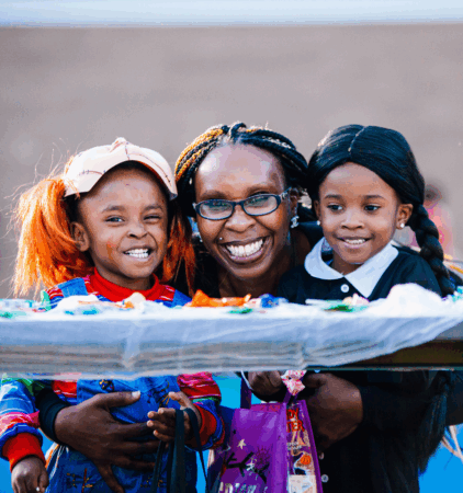 young african american children dressed in costume being hugged by woman