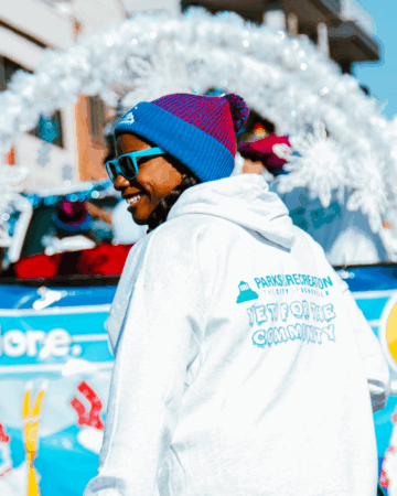 parks and recreation employee wearing white hoodie walks in parade