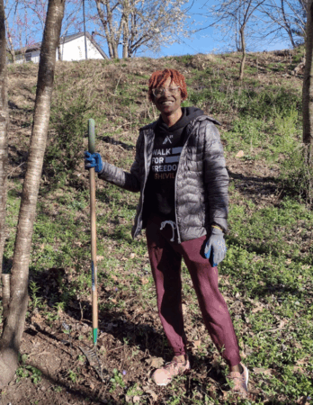 volunteer with rake removes undergrowth in wooded area