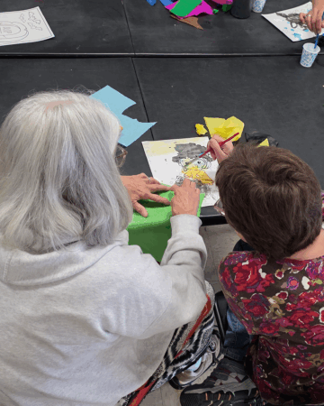 woman with gray hair helps young child paint picture