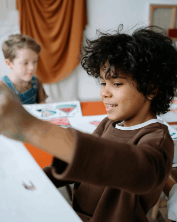 young boy holds up his project from art class