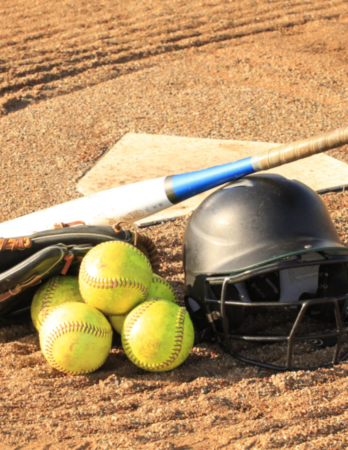  softballs, softball glove, bat, and helmet stacked in front of home plate