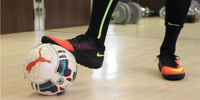 Foot on top of futsal ball on a gym floor