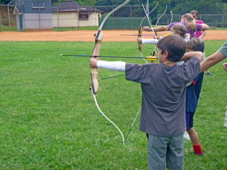 instructor teaching youth how to draw a bow in archery class