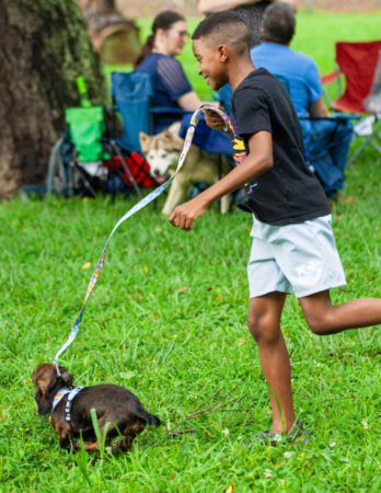 kid running through grass with dog on leash