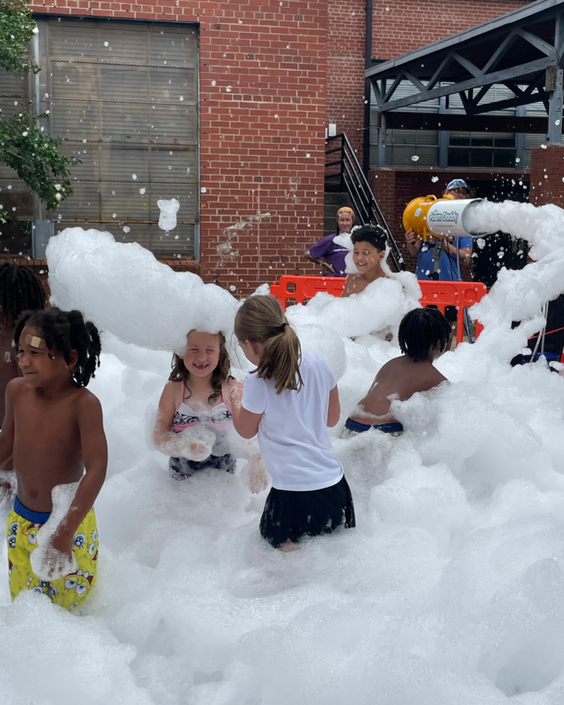  teenagers covered in foam from a foam launcher in front of a community center